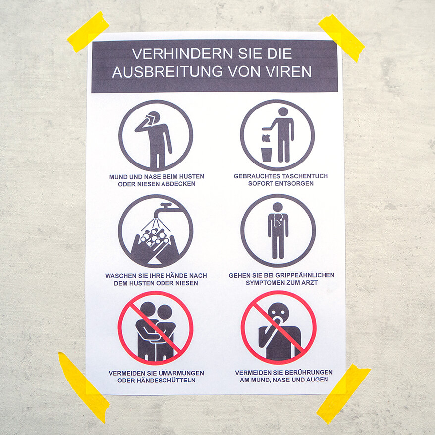 An einer grauen Wand in Betonoptik ist mit gelbem Klebeband ein Hinweisschild zur Verhinderung der Ausbreitung von Viren befestigt. Foto: Johanna Rundel