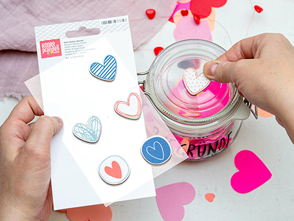 Jemand klebt mit der rechten Hand einen 3D-Aufkleber in Herzform von Knorr Prandell auf ein Vorratsglas. In der linken Hand hält die Person den Aufkleberbogen auf dem sich weitere Herzen befinden. Foto: Johanna Rundel