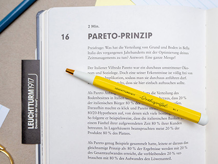 Auf einem grauen Untergrund liegt das blaue Change Journal von Leuchtturm1917. Die Seite über das Paretoprinzip ist aufgeschlagen. Auf dem Journal liegt ein gelber Drehgriffel. Foto: Johanna Rundel