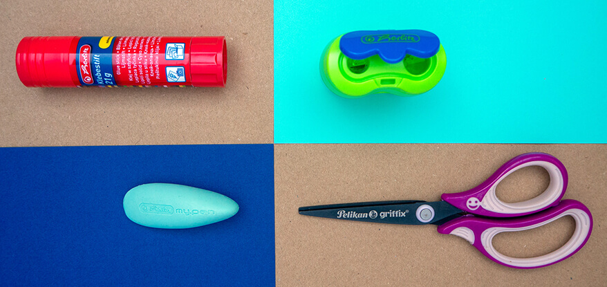 Das Bild ist in vier farbige Segmente aufgeteilt. Im linken oberen, kraftpapierfarbenen Segment liegt ein roter Klebestift von Herlitz. Rechts daneben ist ein blau-grüner Doppelspitzer zu sehen. Im linken unteren Segment befindet sich ein organisch geformter, türkisfarbener Radiergummi. Rechts daneben sieht man eine lila Griffix-Schere von Pelikan. Foto: Johanna Rundel