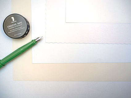 Fünf verschiedene Schreibpapiere von Rössler wurden überlappend aufeinandergelegt, sodass die unterschiedlichen Weißgrade erkennbar sind. Von links ragt ein hellgrüner Füller ins Bild. Darüber liegt ein schwarz-weißes Washitape. Foto: Johanna Rundel