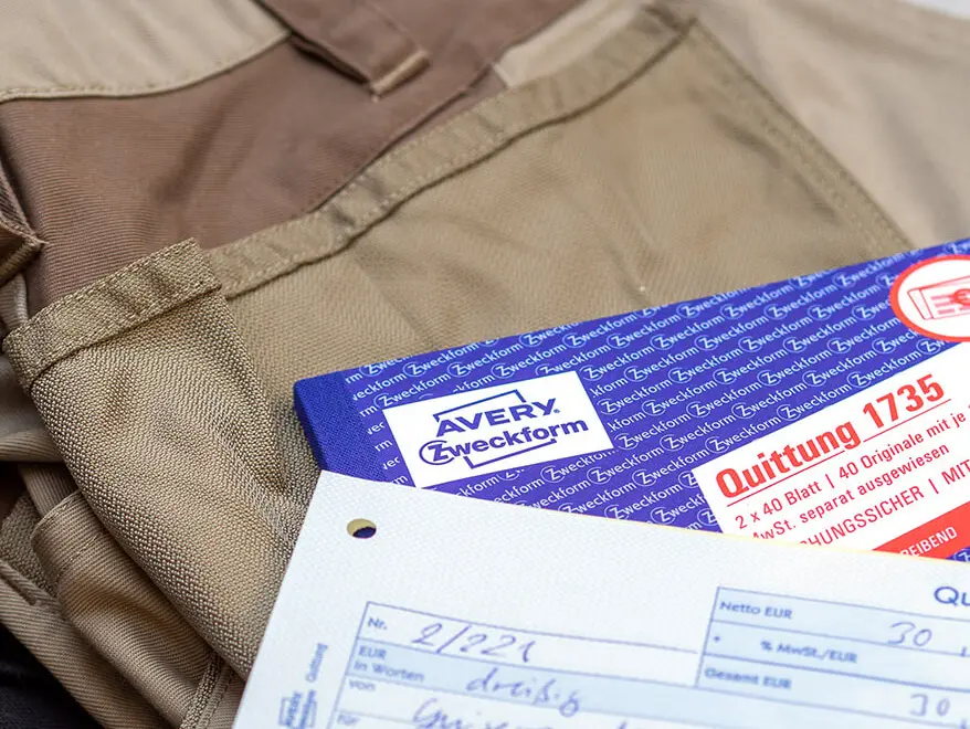 Auf einem Stapel Wäsche liegt ein Quittungsblock von Avery Zweckform. Darauf liegt eine Quittung für eine Reinigung von Arbeitskleidung. Foto: Johanna Rundel