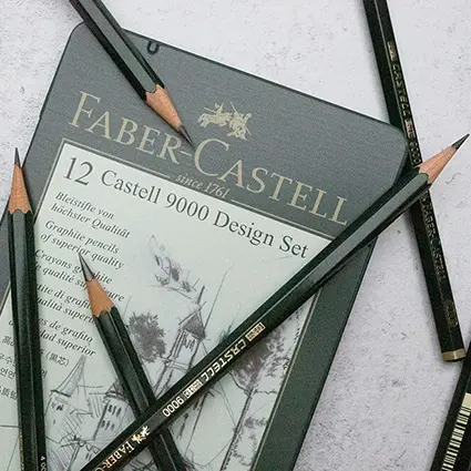 Ein mit Bleistiften gefülltes Metalletui der Marke Faber-Castell liegt auf einem hellgrauen Untergrund. Auf und neben dem Etui liegen weitere dunkelgrüne Bleistifte verstreut. Foto: Johanna Rundel