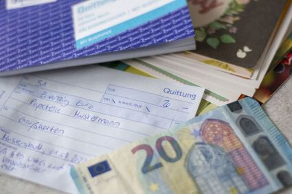 Eine handschriftlich ausgefüllte Quittung liegt zwischen einem 20-Euro-Schein, Grußkarten und einem Quittungsblock von Avery Zweckform.