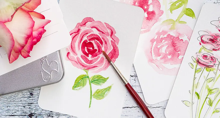 Aquarellpostkarten und ein Metalletui von Hahnemühle liegen auf einem weißen Tisch. 