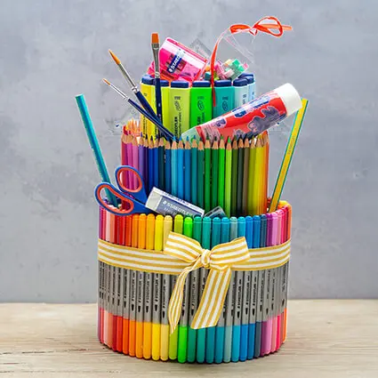 Eine Torte aus verschiedenen Stiften, Schulmaterialien und Markern der Marke Stadtler steht vor einem grauen Hintergrund auf einer Holzunterlage.