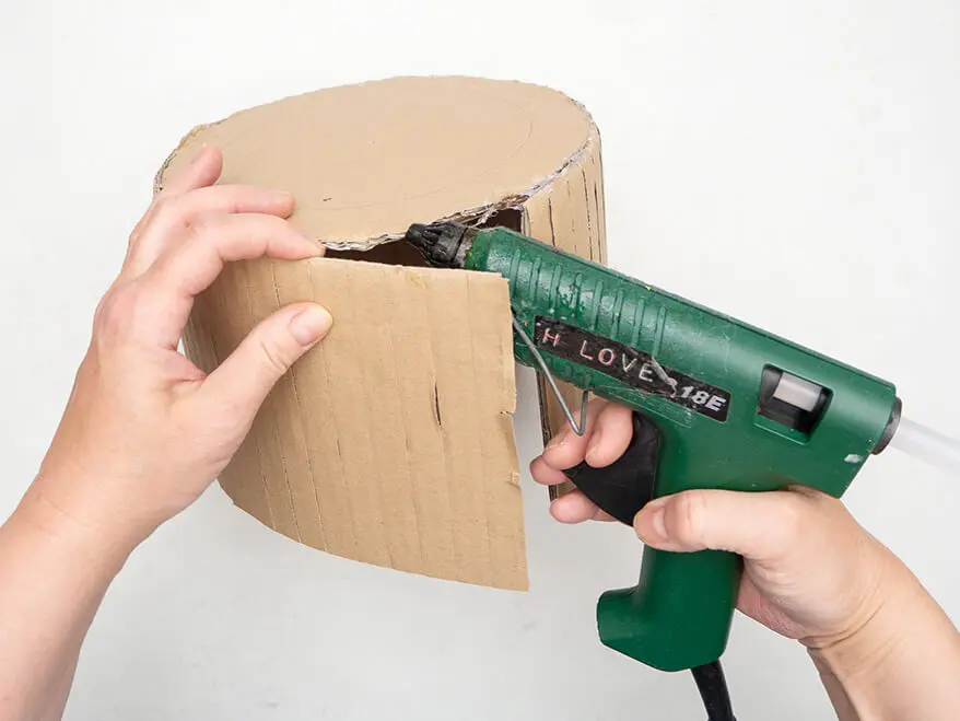 Jemand klebt mit Heißkleber einen Streifen Pappe an die Kante eines Pappkreises.