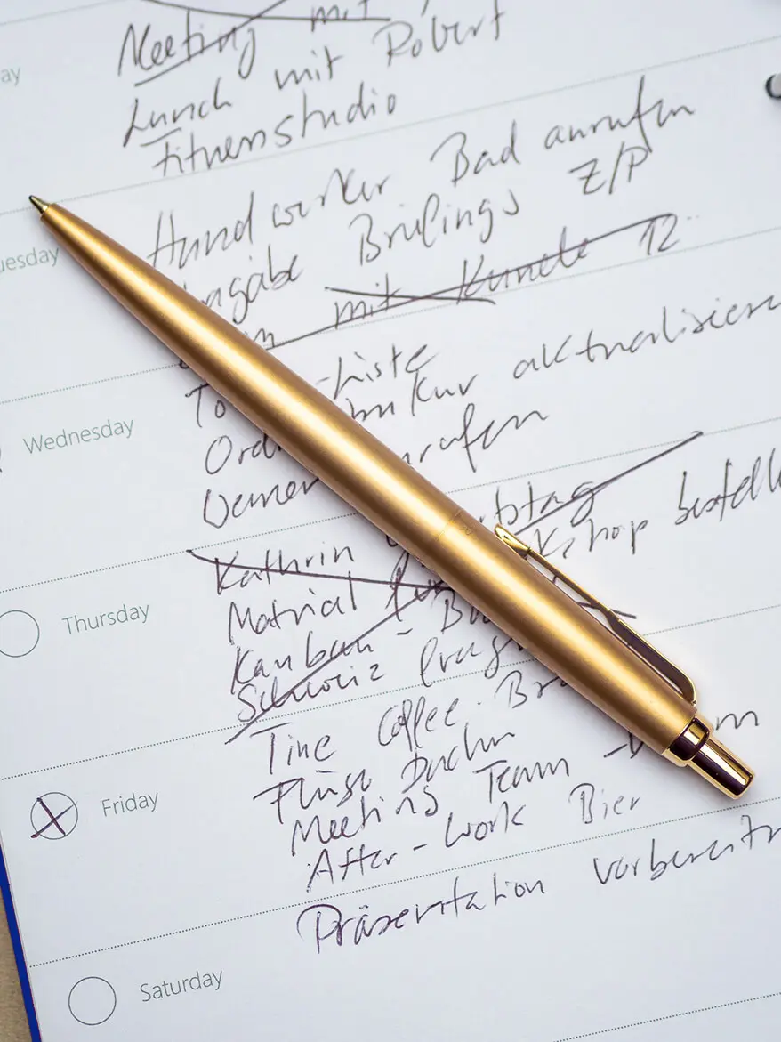 Auf einer beschriebenen Seite eines Terminkalenders, liegt ein goldener Kugelschreiber von Parker. Foto: Johanna Rundel