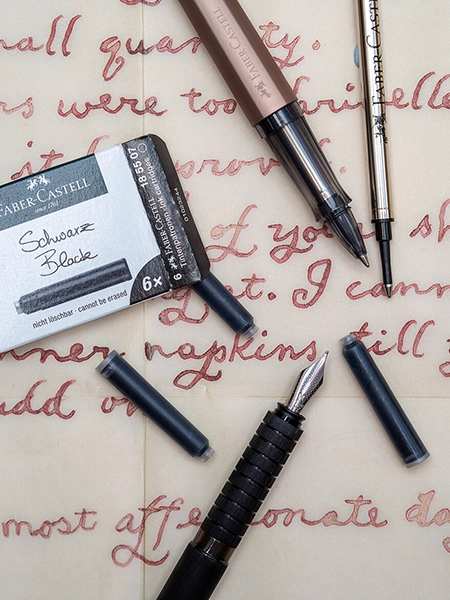 Auf einem beschriebenen Blatt Papier liegen ein Füller und ein Tintenroller von Faber-Castell. Drumherum liegen eine Tintenroller-Mine und mehrere schwarze Tintenpatronen verstreut. Foto: Johanna Rundel