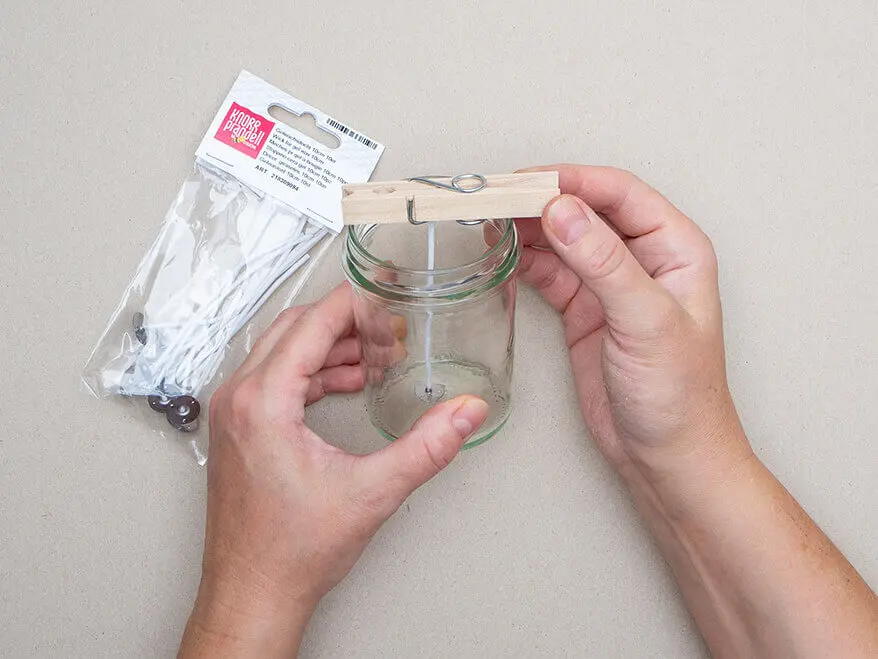 Jemand fixiert einen Runddocht von KNORR prandell mit einer Holzwäscheklammer mittig in einem leeren Marmeladenglas. Foto: Johanna Rundel