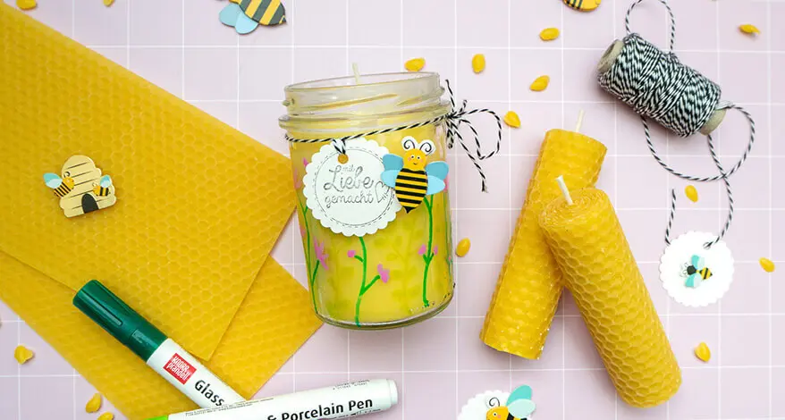 Auf einem rosa Untergrund liegen Bienenwachsplatten, eine DIY-Bienenwachskerze im Glas und gerollte Bienenwachskerzen. Drumherum sind Bastelmaterialien von HEYDA und KNORR prandell verteilt. Foto: Johanna Rundel