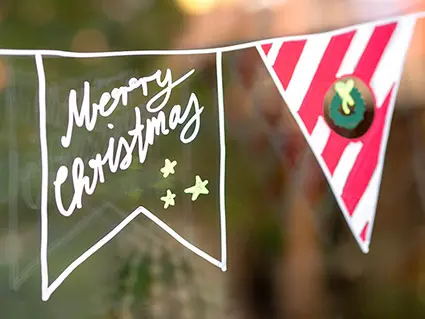 Auf ein Fenster ist mit Kreidemarkern von edding eine Wimpelkette mit weihnachtlichen Motiven und Sprüchen gemalt worden. Foto: Johanna Rundel