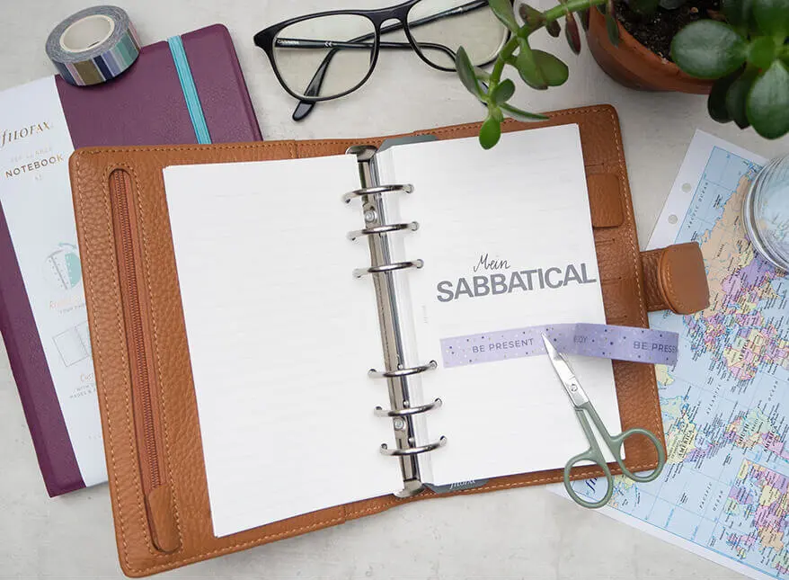 Auf einem Tisch liegt ein aufgeschlagener Filofax. Auf der Seite steht in schwarzen Buchstaben: „Mein Sabbatical“. Foto: Johanna Rundel