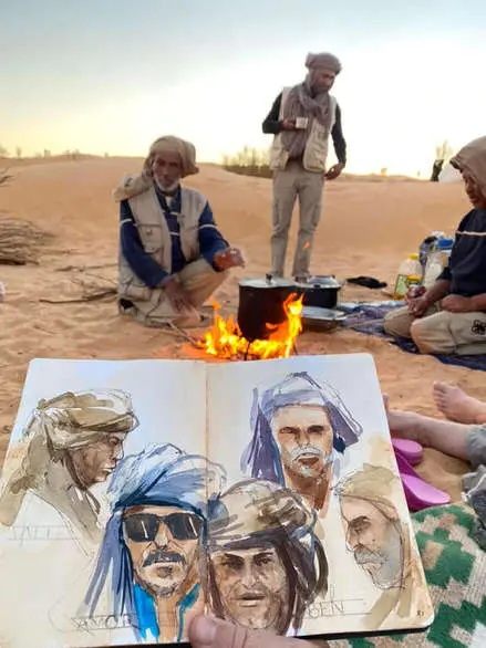 Blick auf und über ein Hahnemühle-Skizzenbuch von Jens Hübner. Dahinter ist das Motiv in echt zu sehen. Eine Wüstenszene mit Feuer und Beduinen.