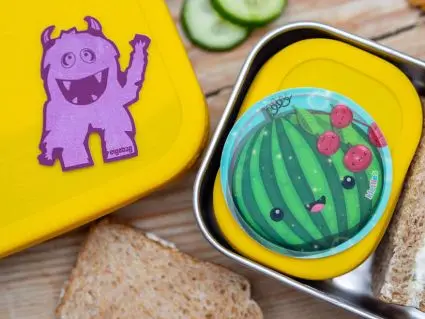 Zwei Edelstahlbrotdosen von ergobag mit gelben Silikondeckeln. Darauf ein Reflektorsticker und ein Klettie mit Melonenmotiv. Foto: Johanna Rundel