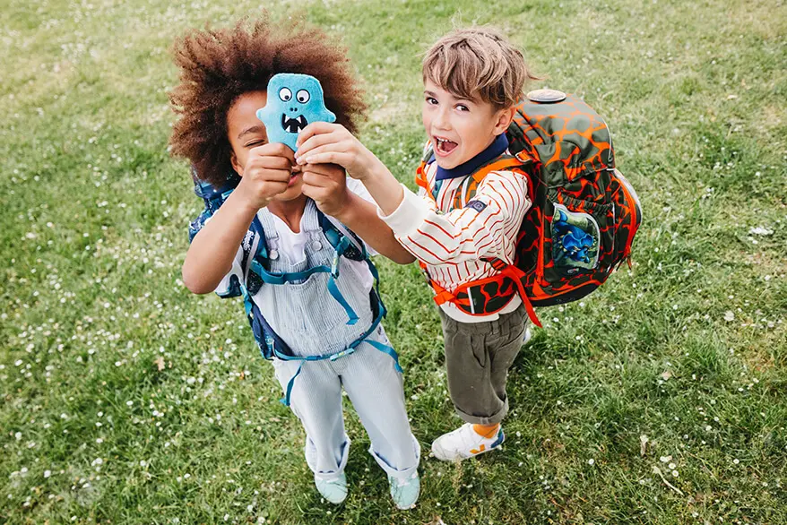 Zwei Grundschüler stehen auf einer grünen Wiese und halten einen blauen Hangie aus Plüsch von ergobag in die Kamera. Foto: Johanna Rundel