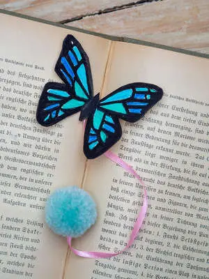 Ein Lesezeichen in Form eines blauen Schmetterlings mit einer Bommel am Ende eines rosa Satinbandes liegt auf einem aufgeschlagenen, vergilbten Buch. Foto: Johanna Rundel
