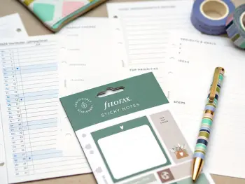 Viele verschiedenen Planer, Einleger, Sticky-Notes und ein Stift von Filofax liegen auf einer grauen Unterlage verteilt. Foto: Johanna Rundel 