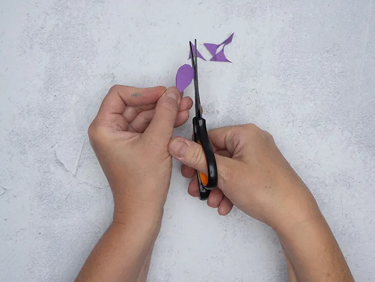 Jemand schneidet mit einer griffix-Schere von Pelikan einen Halbkreis von einem gefalteten Stück lila Papier ab. Foto: Johanna Rundel