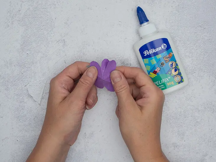 Jemand klebt mit Bastelkleber von Pelikan nebeneinanderliegende Blütenblätter einer lila Papierblume aufeinander. Foto: Johanna Rundel