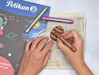 Jemand malt mit colorella-Metallic-Markern von Pelikan Muster auf ein Papier-Ei aus schwarzem Tonpapier. Foto: Johanna Rundel