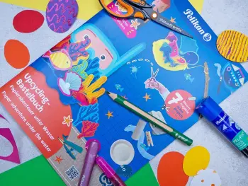 Das Upcycling-Bastelbuch zum Thema Unterwasserwelt von Pelikan liegt zwischen verschiedenen Bastelmaterialien auf einem grauen Untergrund. Foto: Johanna Rundel