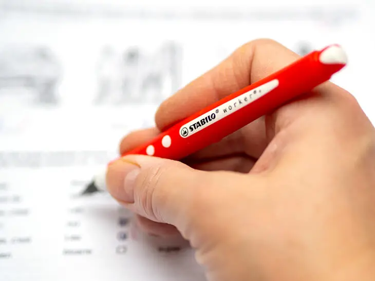 Eine Hand schreibt mit einem roten Stift von Stabilo in ein liniertes Schulheft. Foto: Johanna Rundel