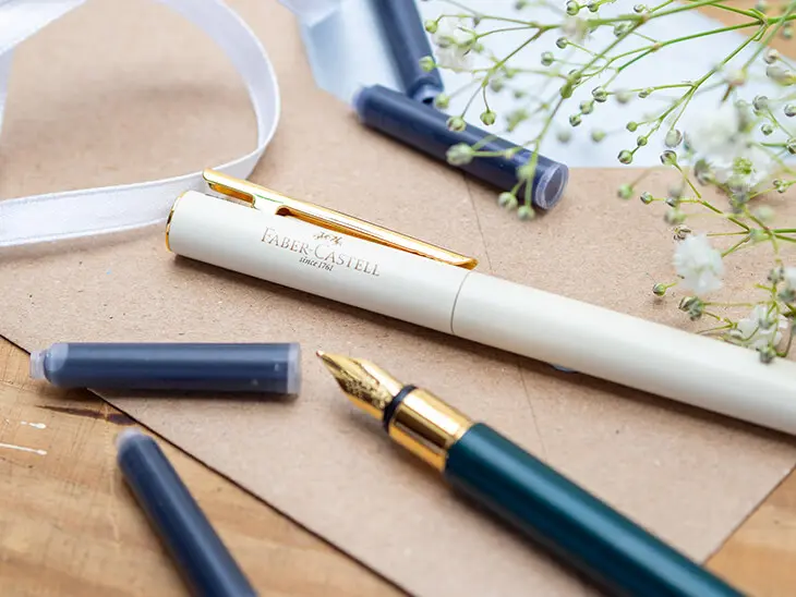 Zwei elegante Füller von Faber-Castell liegen auf einem Kraftpapier-Briefumschlag. Verschiedene Tintenpatronen sind darum verteilt. Foto: Johanna Rundel
