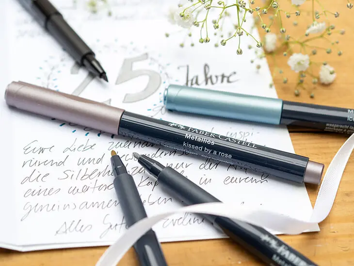 Verschiedene Metallic-Marker von Faber-Castell liegen auf einer geschriebenen Glückwunschkarte zur Silberhochzeit, Foto: Johanna Rundel