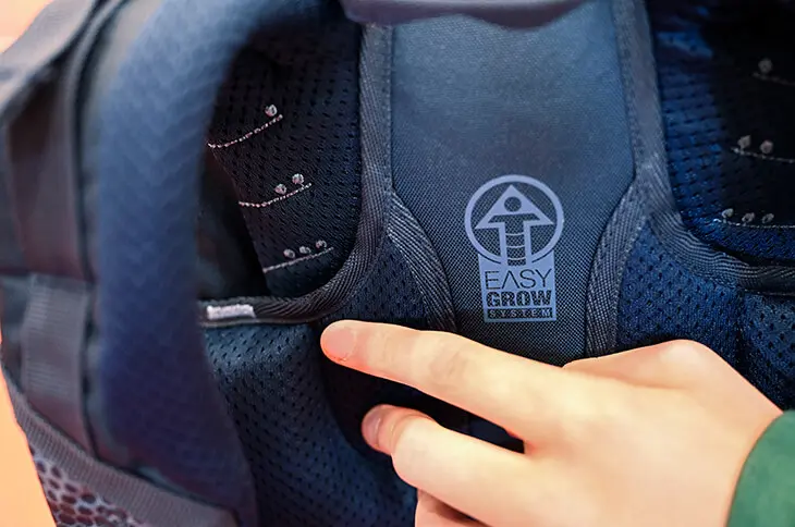 Jemand verstellt das Tragesystem an einem blauen Schulrucksack von coocazoo.