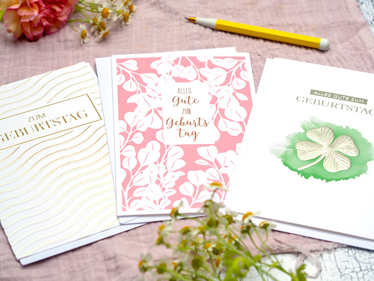 Drei klassisch-elegante Glückwunschkarten zum Geburtstag von ABC Grußkarten, liegen auf einer rosa Tischdecke. Foto: Johanna Rundel