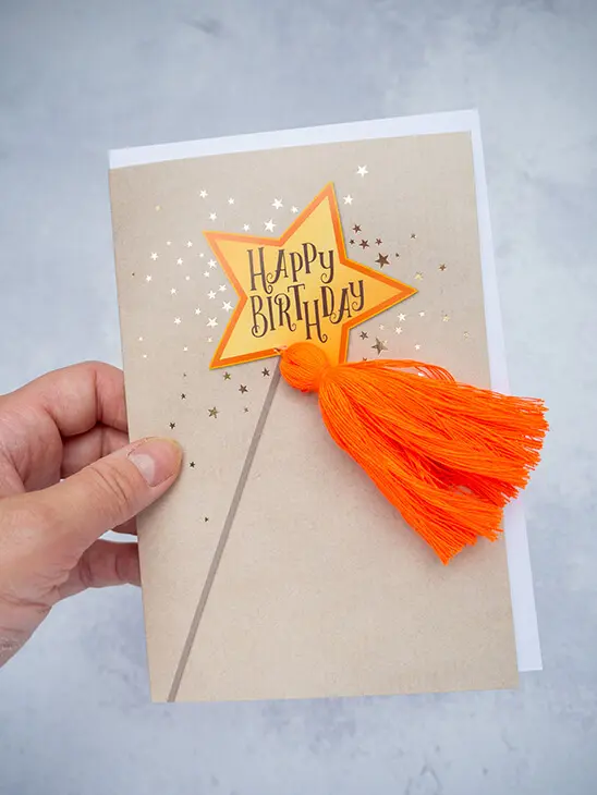 Jemand hält eine Geburtstagskarte mit Zauberstab und orangener Troddel von ABC Grußkarten in die Kamera. Foto: Johanna Rundel