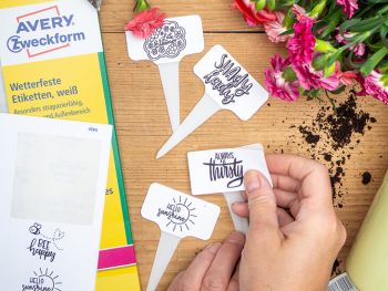 Jemand beklebt weiße Pflanzenstecker mit Aufklebern von Avery Zweckform auf denen verschiedene Letterings aufgebracht wurden. Foto: Johanna Rundel)