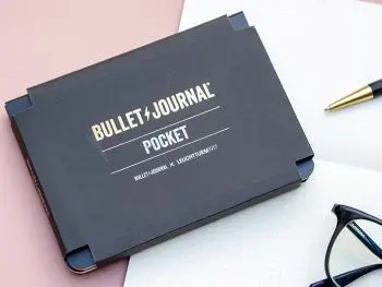 Das Produkt Bullet Journal Pocket von LEUCHTTURM1917 liegt auf einer rosa Schreibtischunterlage. Daneben sind eine Brille und ein Drehgriffel zu sehen. Foto: Johanna Rundel