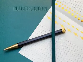 Auf einem dunkelgrünen Bullet Journal von LEUCHTTURM1917 liegen ein aufgefalteter Stickerbogen und ein Drehgriffel. Foto: Johanna Rundel