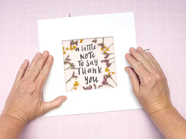 Jemand legt ein weißes Passepartout auf einen rosa Karton, auf den mit Kreativmarkern von Faber-Castell ein Satz gelettert wurde. Foto: Johanna Rundel