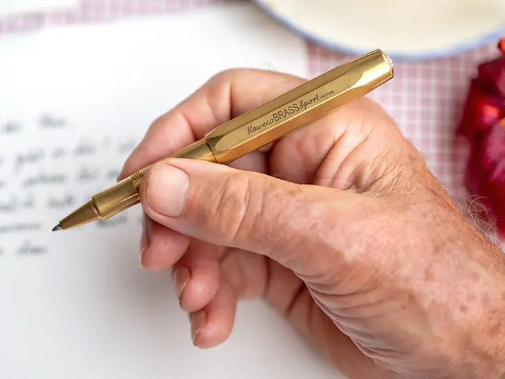 Die Hand eines älteren Mannes hält einen goldenen "Brass Sport" Füller von Kaweco, um einen Brief an sein Enkelkind zu schreiben. Foto: Johanna Rundel