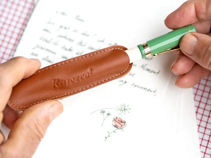 Jemand zieht einen grün-weißen Füller von Kaweco aus einem braunen Lederetui. Foto: Johanna Rundel