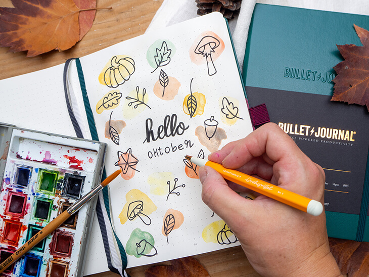 Monatsdeckblatt für Oktober in einem Bullet Journal von LEUCHTTURM1917. Das Motiv: gezeichnete Herbstmotive in Aquarell-Farbklecksen. Foto: Johanna Rundel