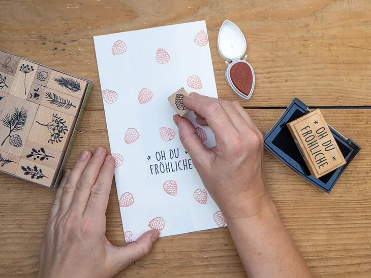 Jemand stempelt bronzefarbenen Zapfen auf eine weiße Papiertüte von HEYDA. Foto: Johanna Rundel