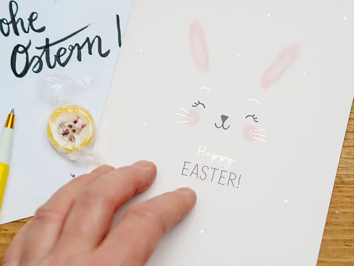 Jemand legt seine Hand auf eine Ostergrußkarte von Grafik Werkstatt auf der „Happy Easter“ steht. Foto: Johanna Rundel