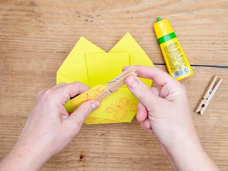 Jemand klebt ein Osternest aus gelbem Papier von HEYDA zusammen und fixiert die Klebestelle mit einer Wäscheklammer von KNORR Prandell. Foto: Johanna Rundel