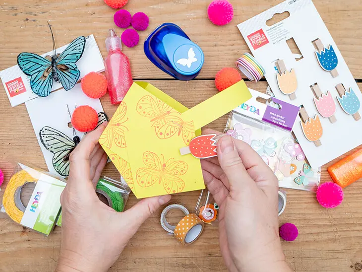 Jemand verziert ein selbstgebasteltes, gelbes Osternest mit Materialien von HEYDA und KNORR prandell. Foto: Johanna Rundel