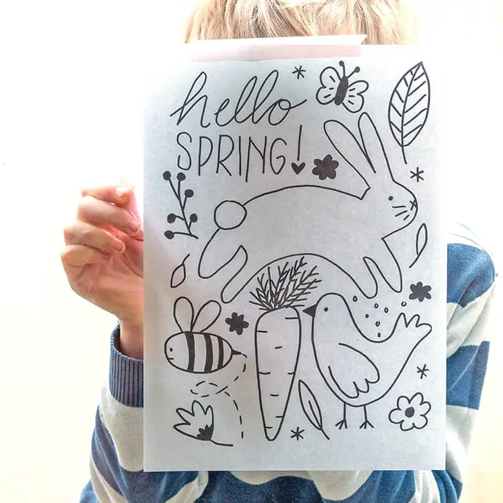 Ein Junge im Grundschulalter klebt mit Washitape eine Fensterbild-Vorlage mit Frühlingsmotiven von außen an eine Fensterscheibe. Foto: Johanna Rundel