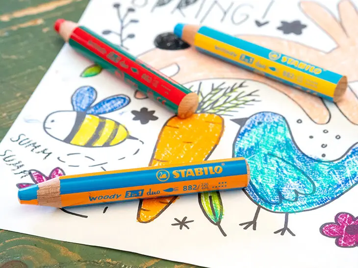 Drei Woody 3in1-Buntstifte von STABILO liegen auf einer bunt ausgemalten frühlingshaften Fensterbildvorlage für Kinder. Foto: Johanna Rundel