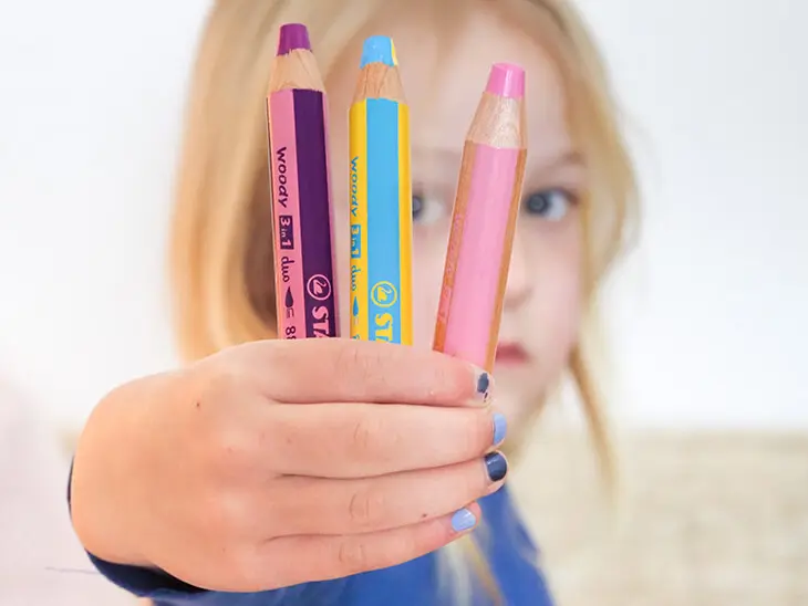 Ein kleines Mädchen mit blonden Haaren hält drei Woody 3in1-Buntstifte von STABILO in die Kamera. Foto: Johanna Rundel