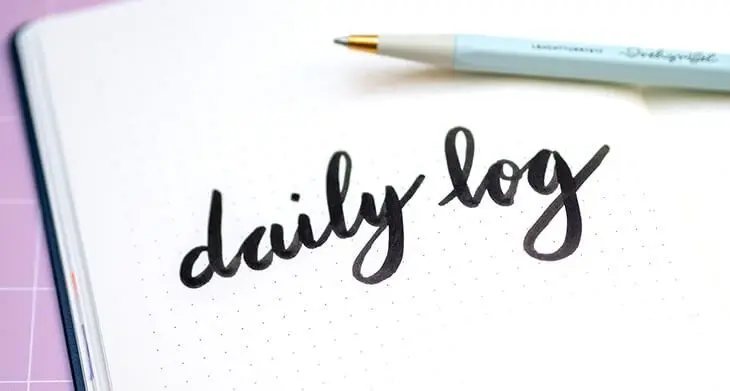 In einem aufgeschlagenen Bullet Journal von LEUCHTTURM1917 steht „daily log“ im Handletteringstil. Darauf liegt ein türkiser Drehgriffel. Foto: Johanna Rundel