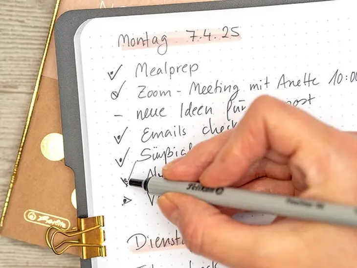 Jemand schreibt mit einem schwarzen Fineliner von Pelikan ein rapid log in ein Notizheft von herlitz. Foto: Johanna Rundel