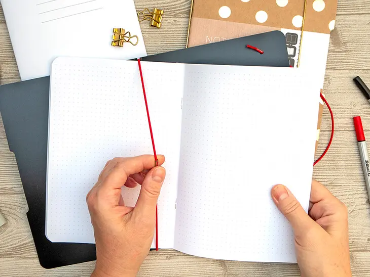 Jemand steckt eine neue Papiereinlage in ein schwarzes my.book flex von herlitz. Daneben liegen zwei Fineliner von Pelikan. Foto: Johanna Rundel