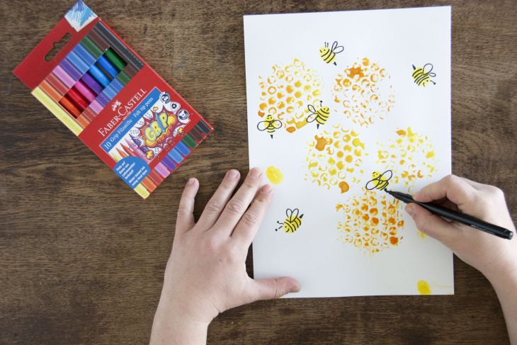 Jemand gestaltet mit schwarzem Filzstift von Faber-Castell gelbe Fingerabdrücke zu kleinen Bienen